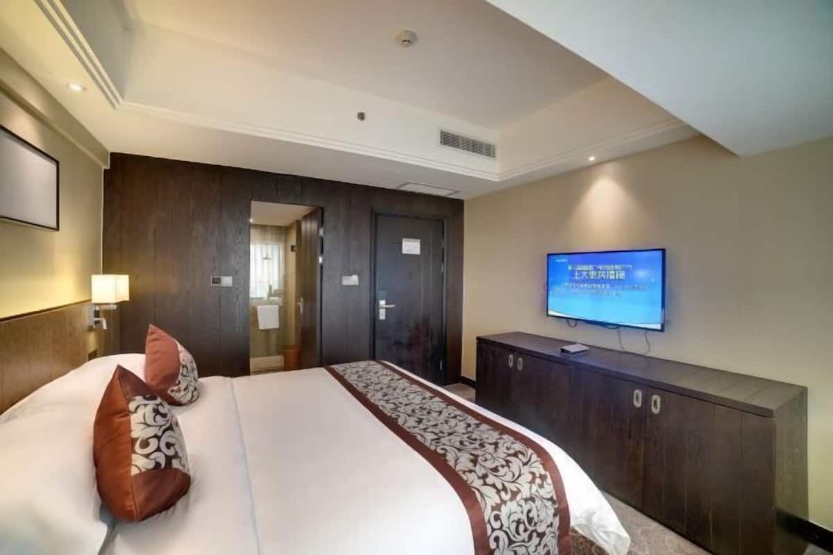 A hotel room with a large bed, a TV mounted on the wall, and a wardrobe.