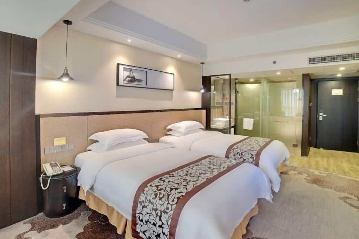 A hotel room with two beds, a bedside telephone, a framed picture on the wall, and a glass shower enclosure.