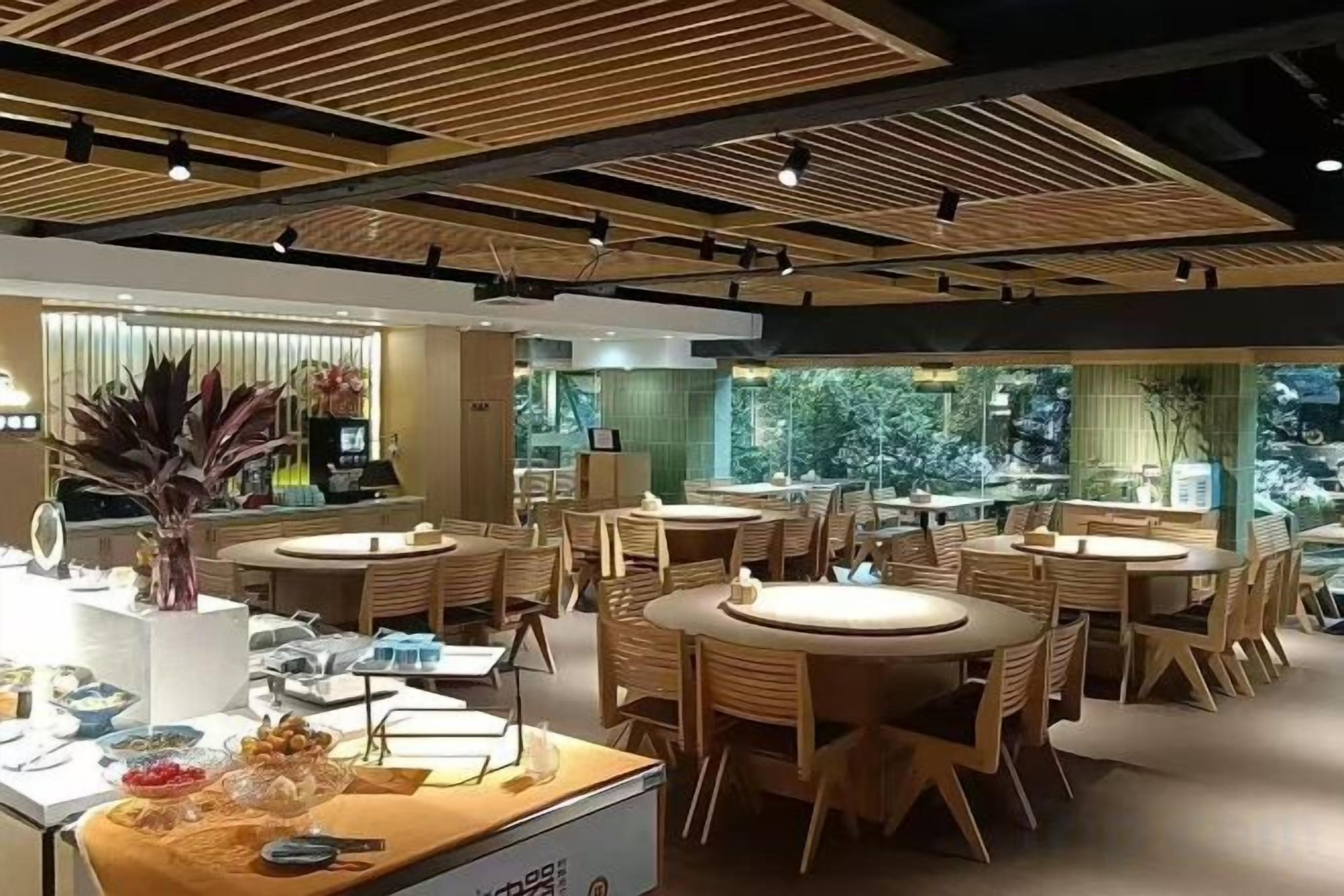 Un comedor moderno con mesas y sillas redondas, una recepción y ventanas grandes.