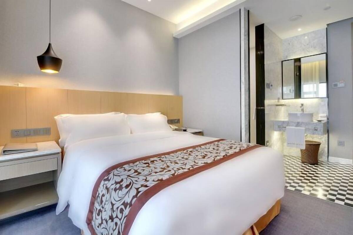 A modern hotel room with a large bed, bedside table, and a bathroom with a mirror and sink.