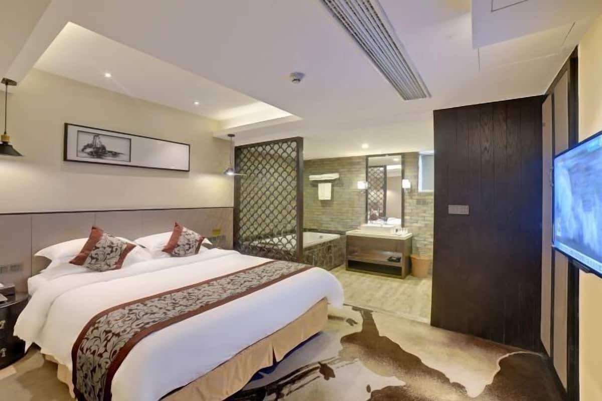 A modern hotel room with a large bed, a separate bathroom, a TV, and a decorative cowhide rug.