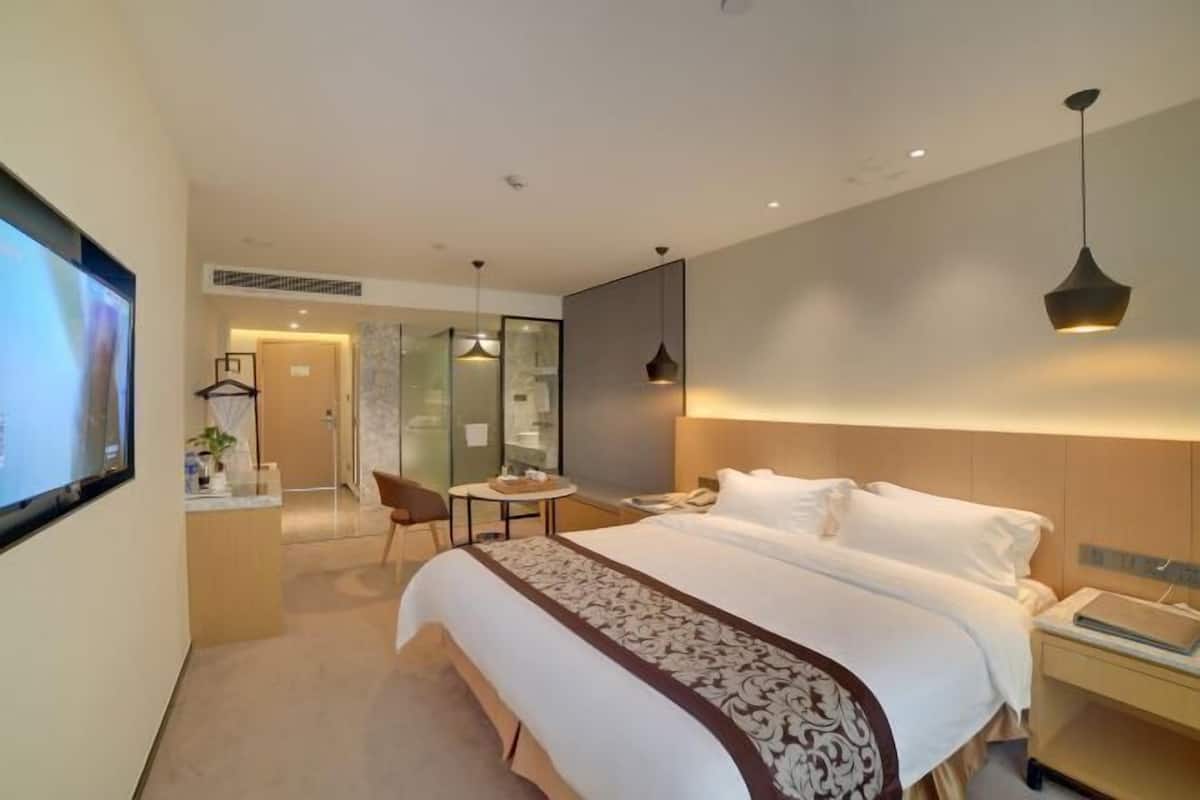 A modern hotel room with a large bed, bedside table, and a desk area.