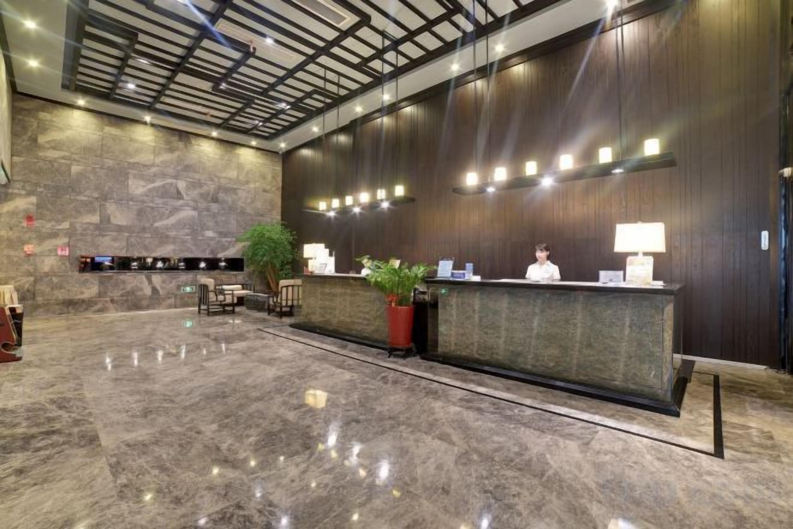 A hotel reception area with a marble floor, a reception desk, a plant, and a large stone wall.