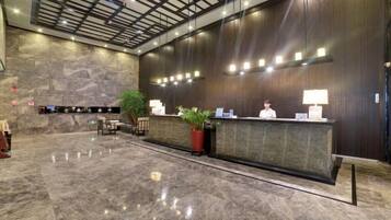 A hotel reception area with a marble floor, a reception desk, a plant, and a large stone wall.