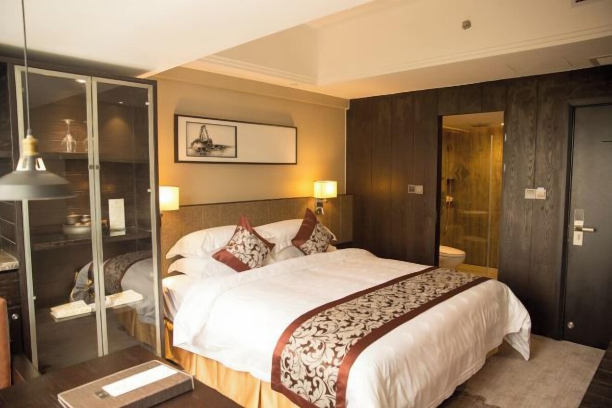 A hotel room with a large bed, bedside lamps, a mirror, and a framed picture on the wall.