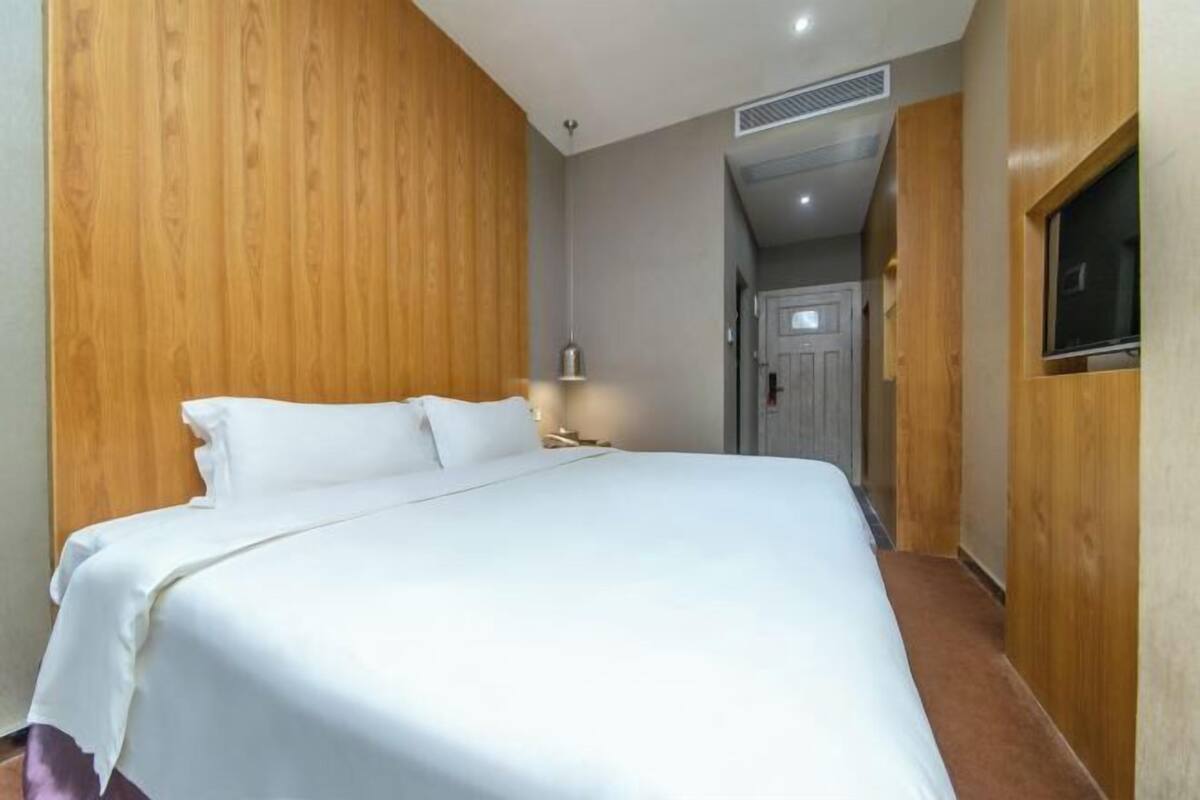 Une chambre d’hôtel avec un grand lit, des murs lambrissés en bois, une lampe de chevet et une porte donnant sur une autre pièce.