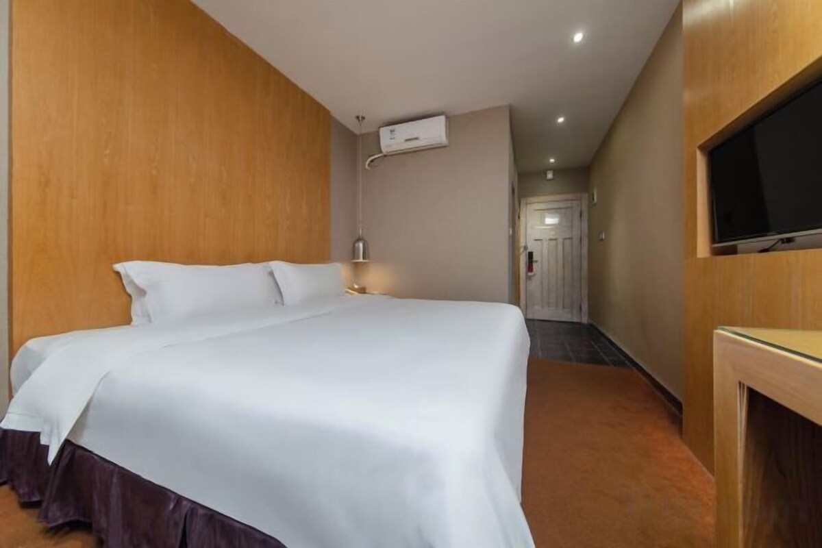 Quarto de hotel com uma cama grande, televisão fixada na parede e painéis de madeira nas paredes.