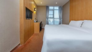 Hotellihuone, jossa on suuri sänky, työpöytä tuolilla, televisio ja ikkuna, jossa on verhot.