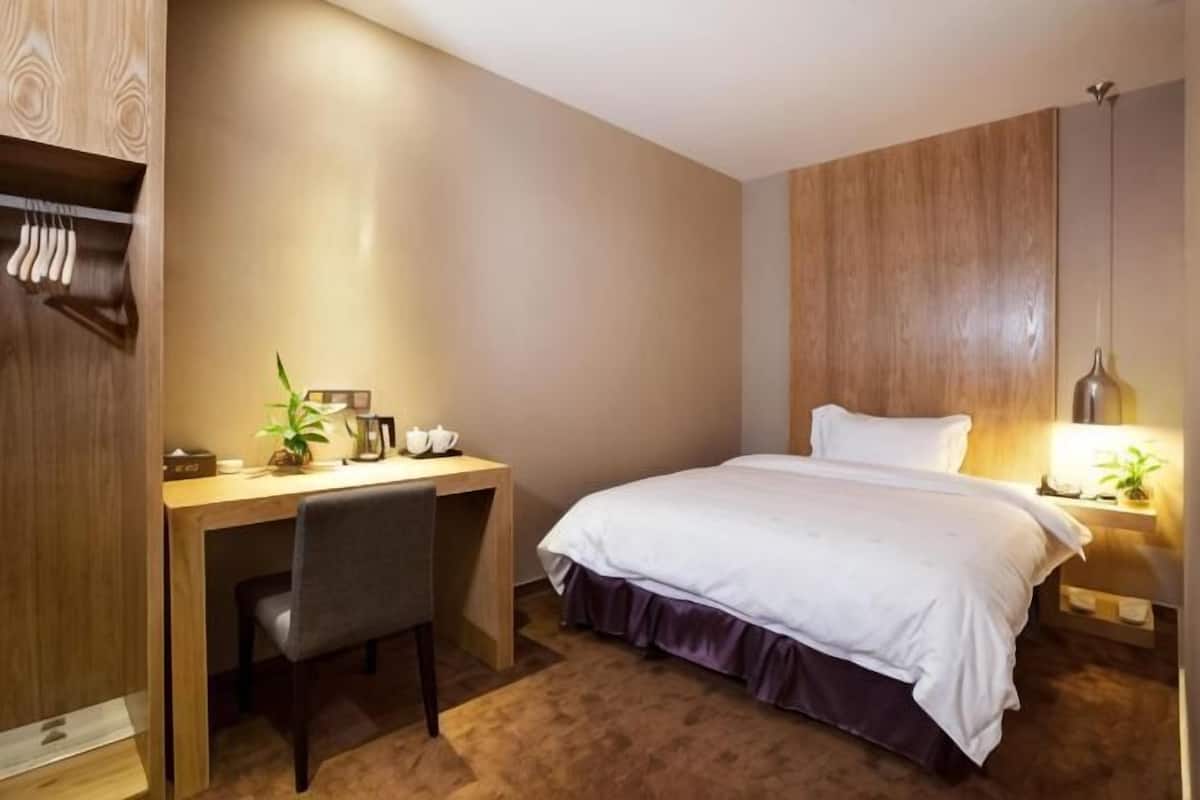 Une chambre d’hôtel comprenant un lit, un bureau, une chaise, une table de chevet et une lampe.