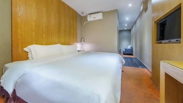 Hotellihuone, jossa on sänky, televisio, yöpöytä ja seinälle asennettu ilmastointilaite.