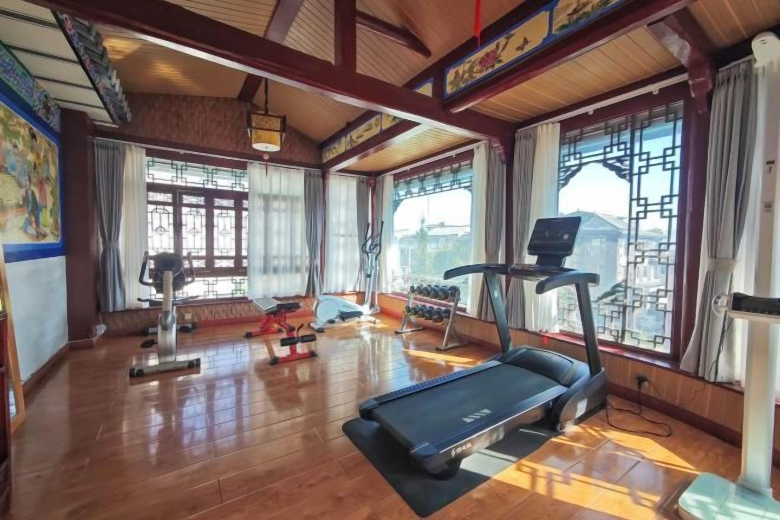 Un gimnasio con equipo de ejercicio, amplias ventanas y piso de madera.