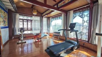 Un gimnasio con equipo de ejercicio, amplias ventanas y piso de madera.