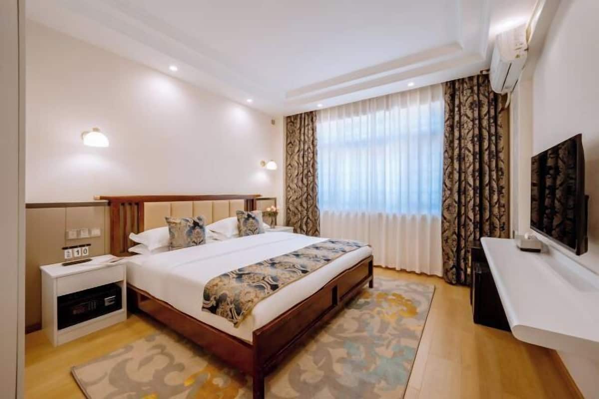A hotel room with a bed, bedside table, TV, and curtains.