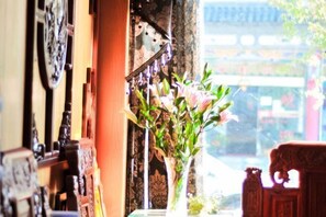 A traditional interior with a wooden cabinet, a vase with flowers, and a view of a building outside. - Jiangnanju Boutique Hotel (Dali City)