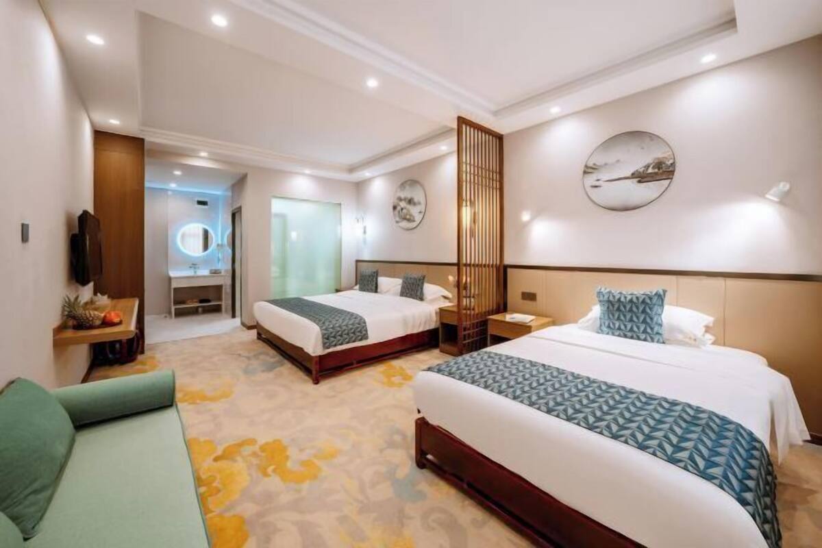 A hotel room with two beds, a sofa, a desk, a mirror, and artwork on the walls.