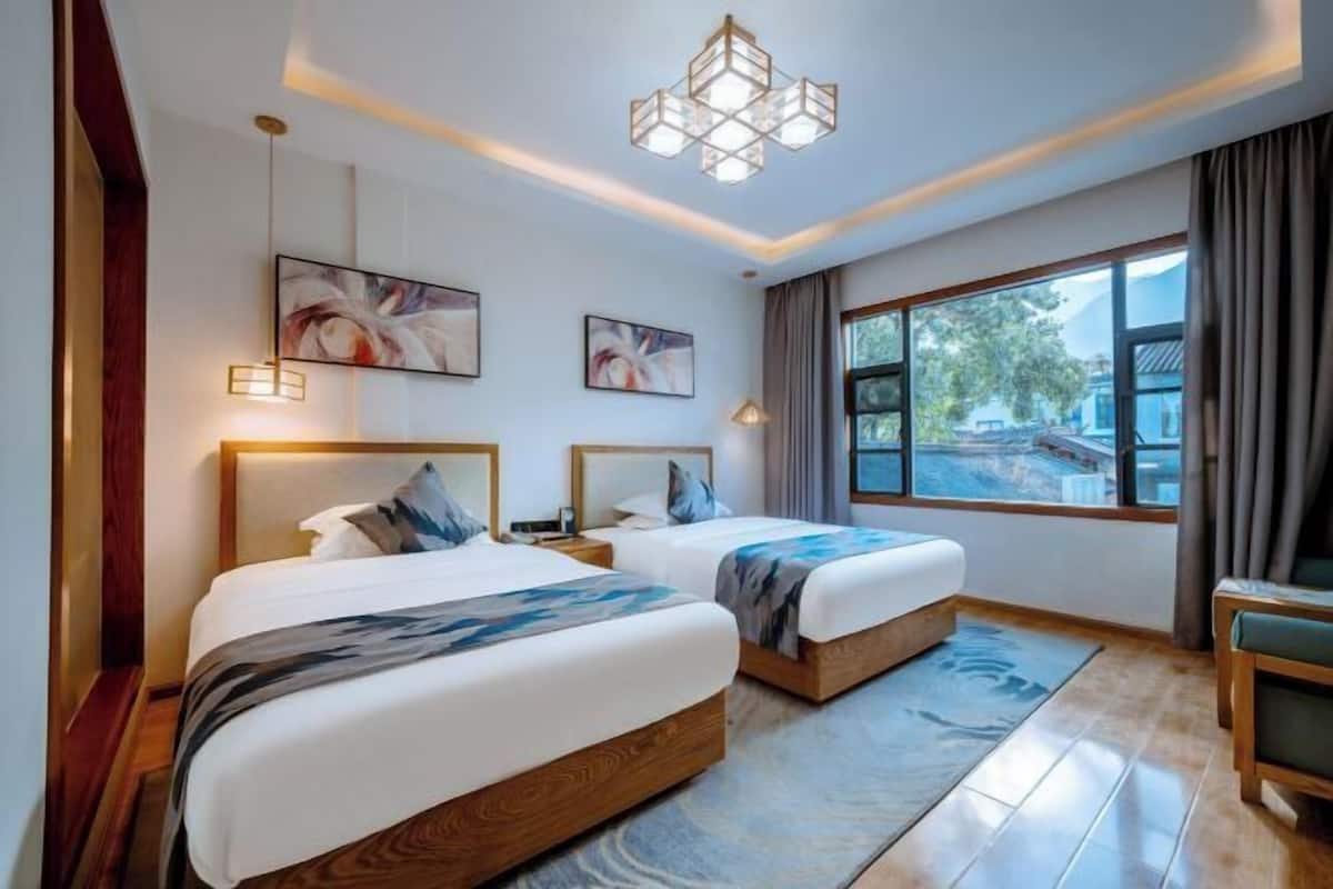 A hotel room with two beds, a large window, and artwork on the walls.