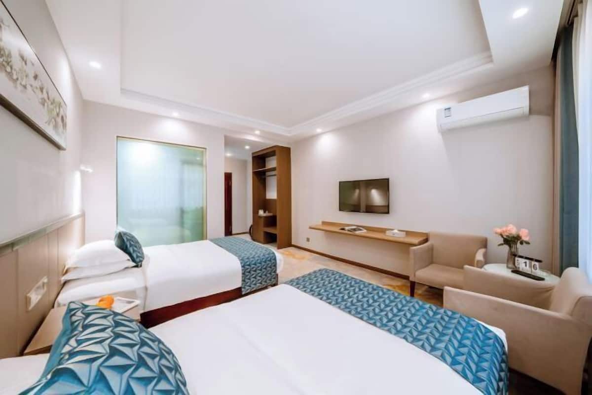 A hotel room with two beds, a sofa, a TV, and a small table with a vase of flowers.