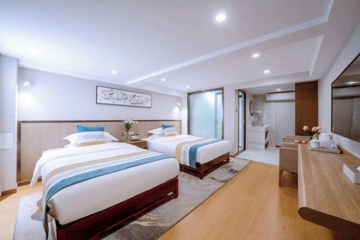 A hotel room with two beds, a desk, a TV, and a bathroom visible through a glass door.