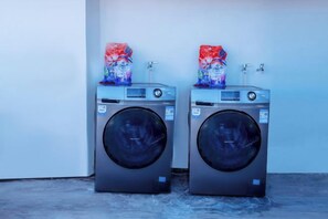 Two front-loading washing machines with a water dispenser on top, placed against a plain wall. - Jiangnanju Boutique Hotel (Dali City)