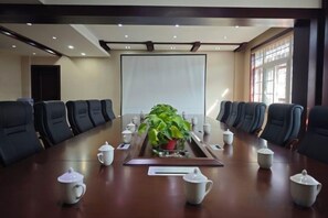 A conference room with a long table, chairs, a projector screen, and a plant.