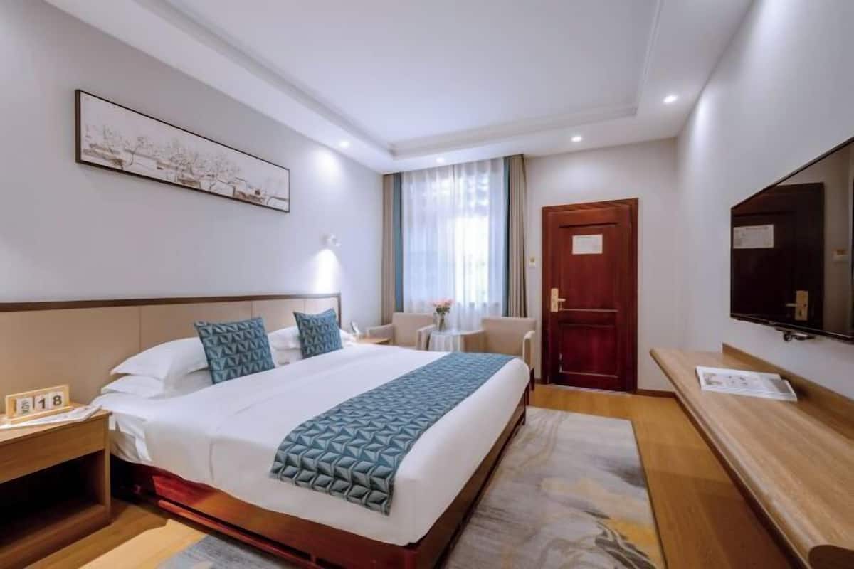 A hotel room with a bed, bedside table, nightstand, TV, and a door.