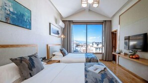 Une chambre d’hôtel avec un grand lit, un plus petit lit, une télévision, une fenêtre donnant sur la ville et un tableau au mur.