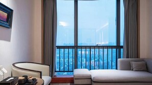 Habitació d'hotel moderna amb un gran finestral que ofereix vistes a la ciutat, un sofà, una taula petita amb una bandeja d'objectes i un quadre al mur.