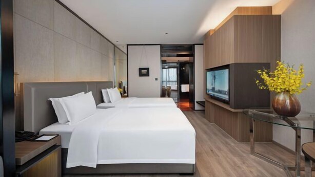 Habitació d'hotel moderna amb un llit gran, una televisió i un ram de flors grogues.