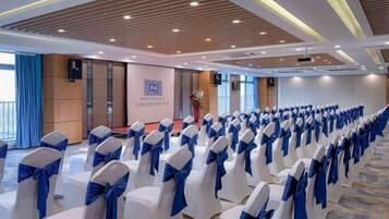 A conference room with rows of white chairs with blue sashes, a stage with a podium, and a banner with text.