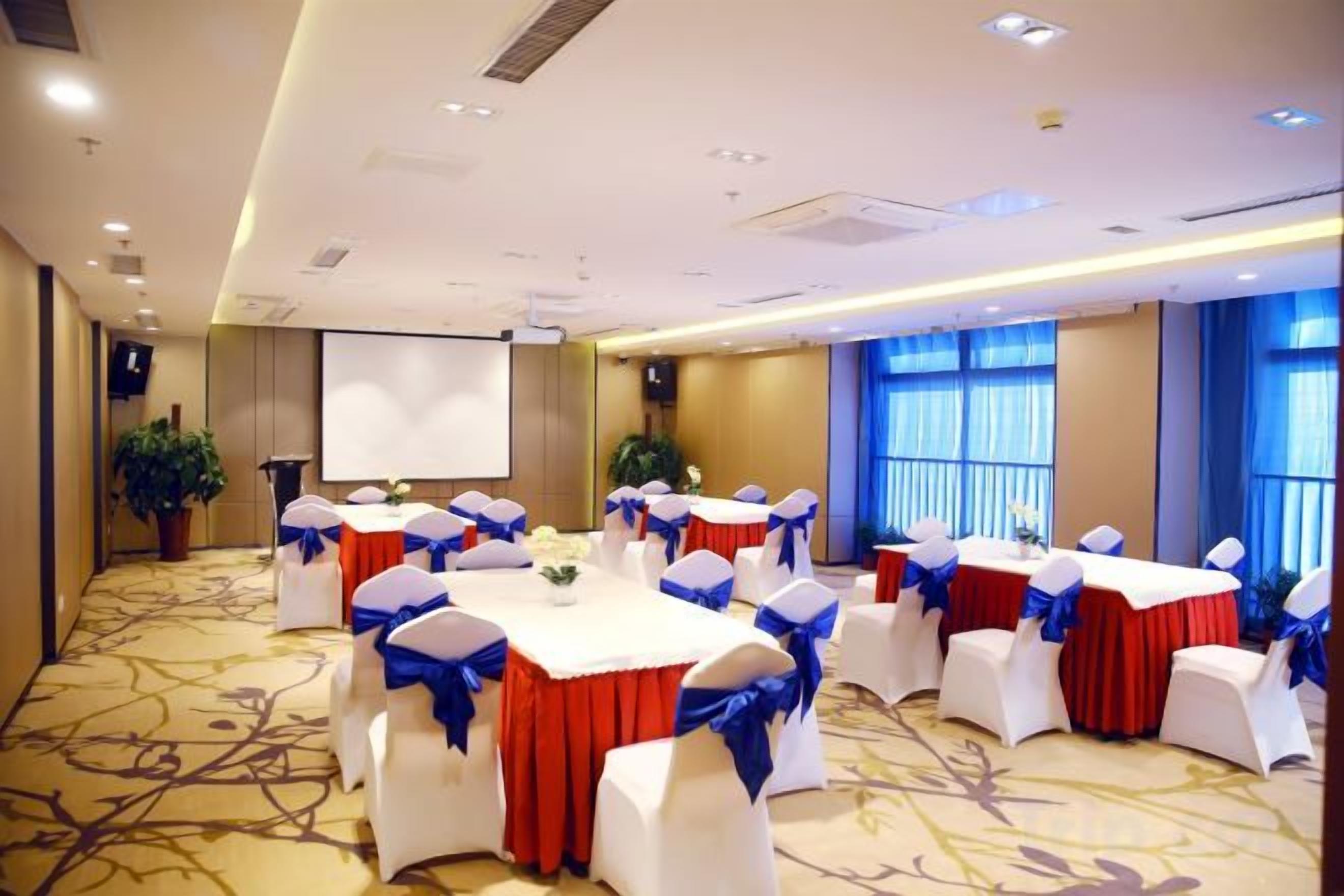 A conference room with round tables, white chairs, and red tablecloths.