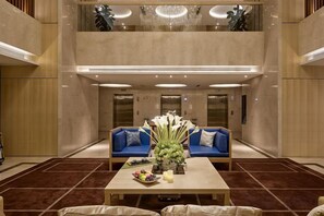 Un vestíbulo con techo alto, un área de estar central con sofás azules, una mesa con un jarrón de flores y una araña.