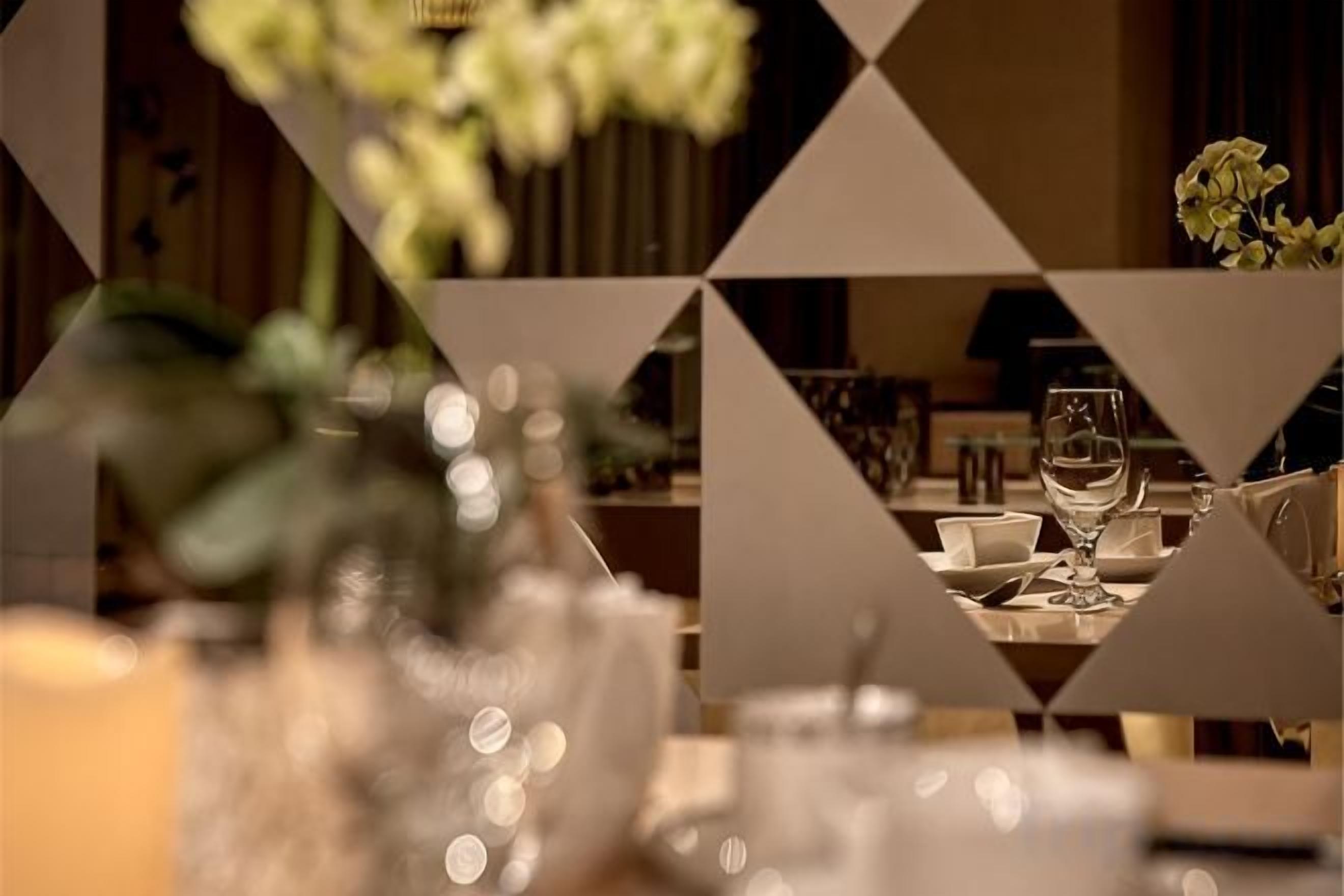 Ein Esstisch mit einem Glas Wasser, einer Blumenvase und einer Wand mit geometrischem Muster.