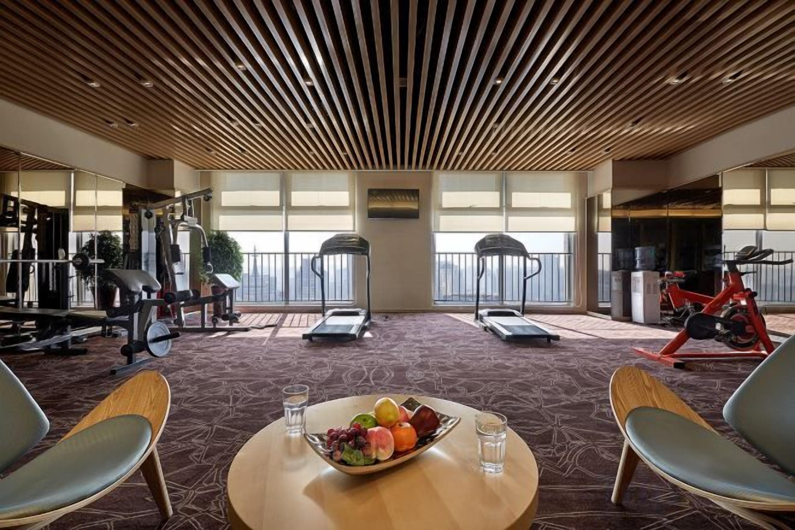 A fitness area with exercise equipment, a table with fruit and water, and a view of the city.