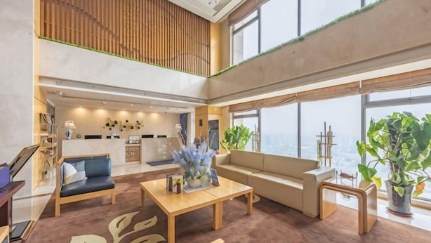 A spacious lobby with a high ceiling, a seating area with a sofa and chairs, a coffee table, and a large window offering a view. - Novlion Hotel (Shijiazhuang)