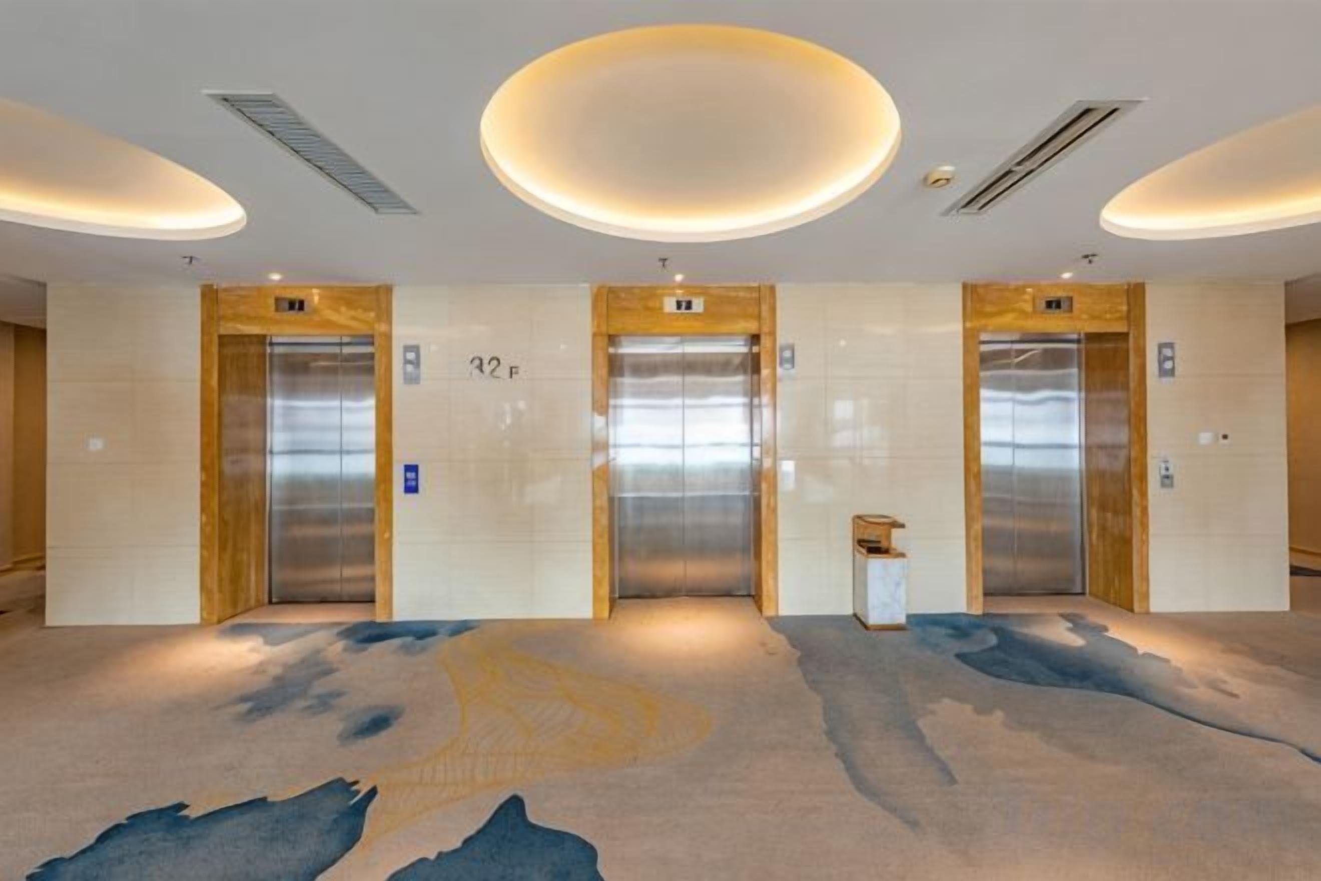 A hotel lobby with three elevators, a patterned carpet, and a modern ceiling design.