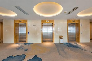 Vestíbulo de hotel con tres ascensores, alfombra estampada y un diseño moderno de techo.
