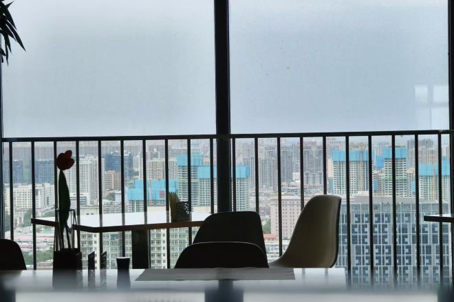 A room with a large window, a balcony with a railing, and a view of a cityscape.