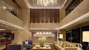 A spacious lobby with a high ceiling, a chandelier, seating areas, and a large window.
