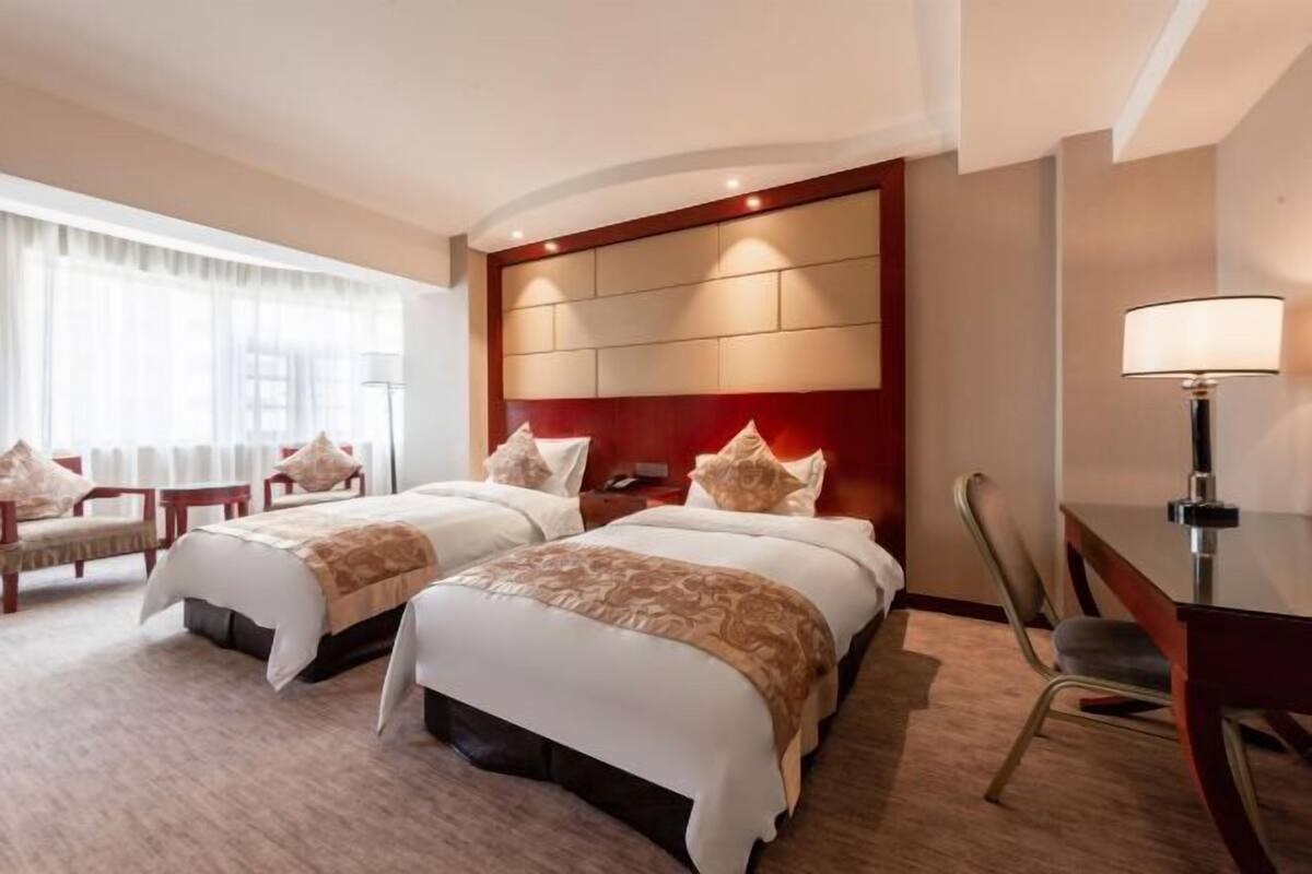 Una habitación de hotel con dos camas, un escritorio, una silla y una lámpara.