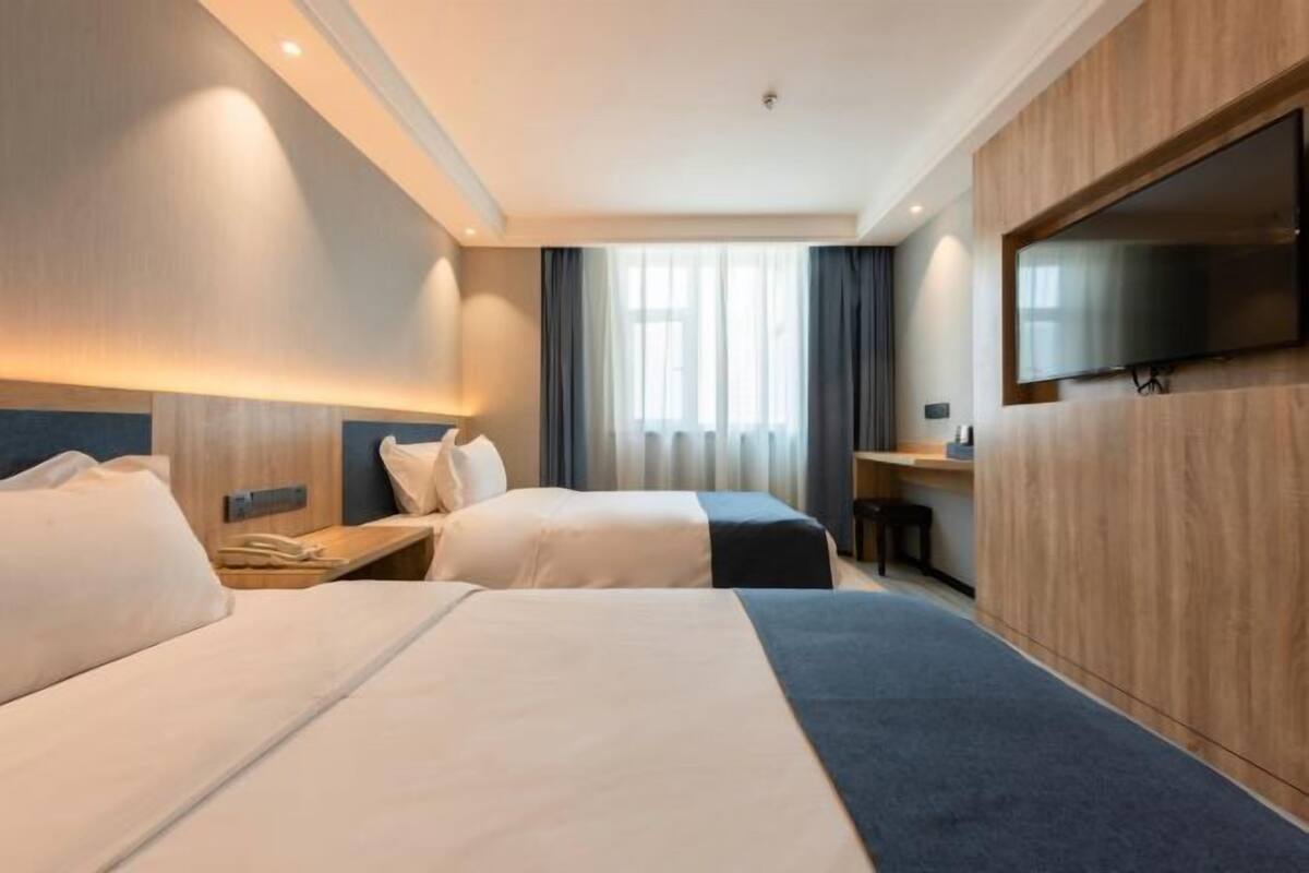 Habitación de hotel con dos camas, televisión instalada en la pared, escritorio y ventana con cortinas.