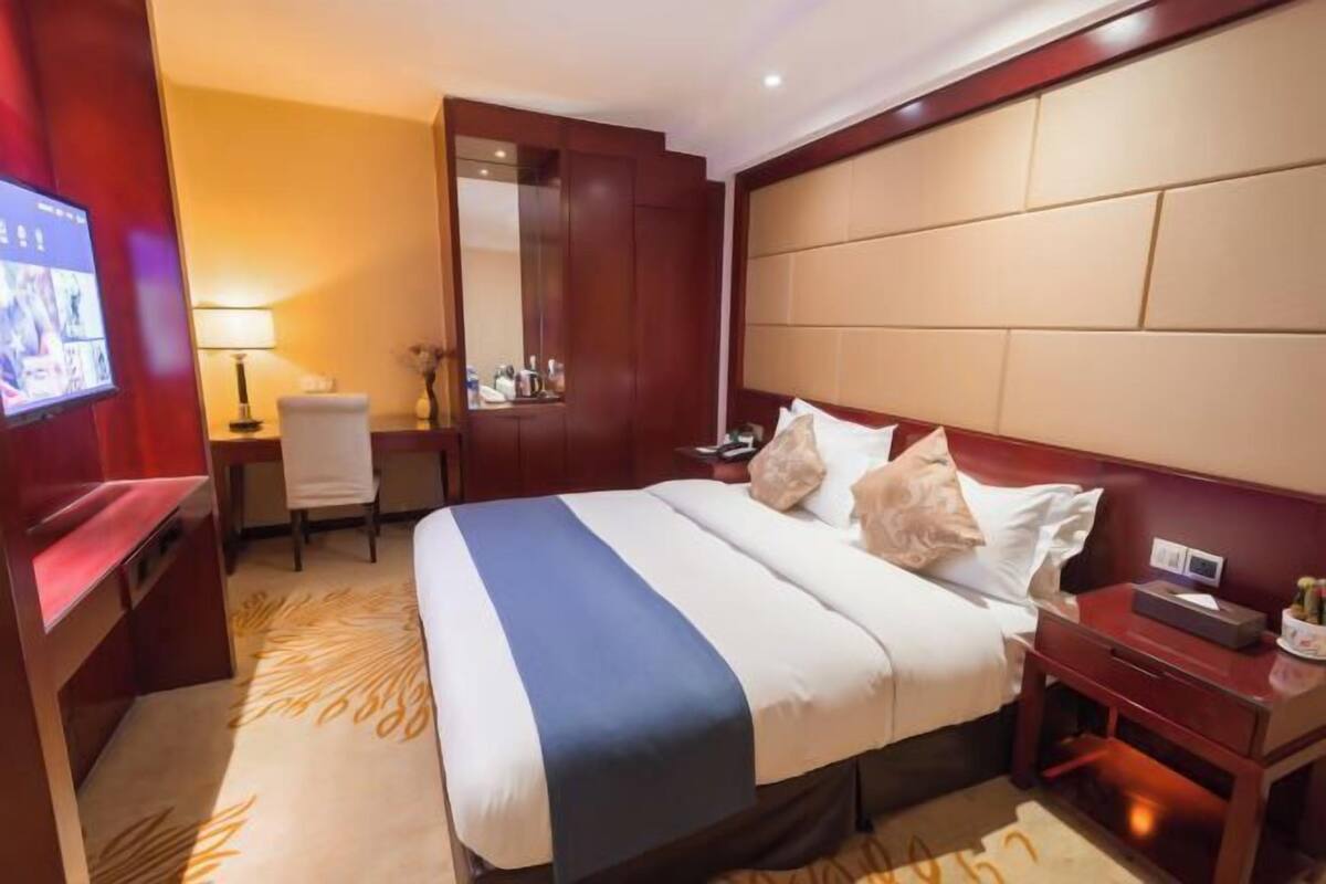 Habitación de hotel con una cama grande, un escritorio, una silla, un televisor y un espejo.