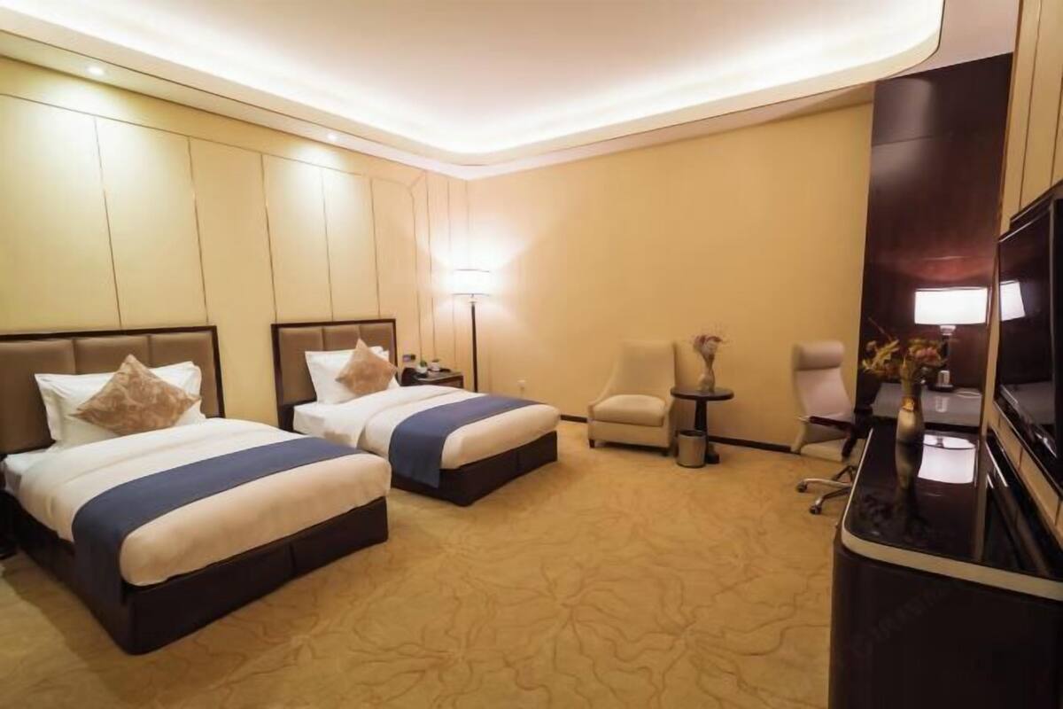 Habitación de hotel con dos camas, un escritorio, una silla, un televisor y una lámpara.