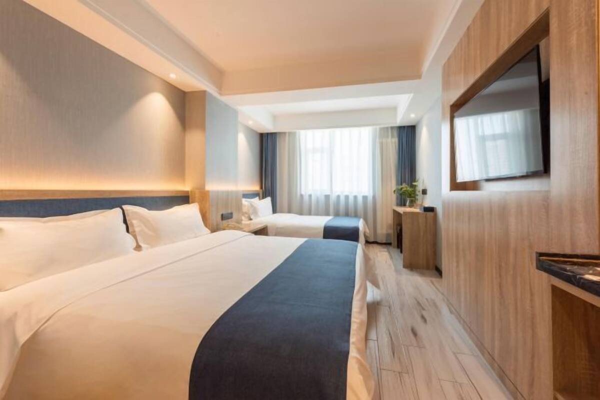 Habitación de hotel con dos camas, televisión, escritorio y ventana con cortinas.