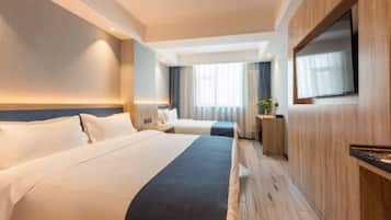 A hotel room with two beds, a TV, a desk, and a window with curtains.