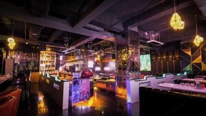 Un área de bar moderna con suelo pulido, mostradores y lámparas geométricas colgantes.