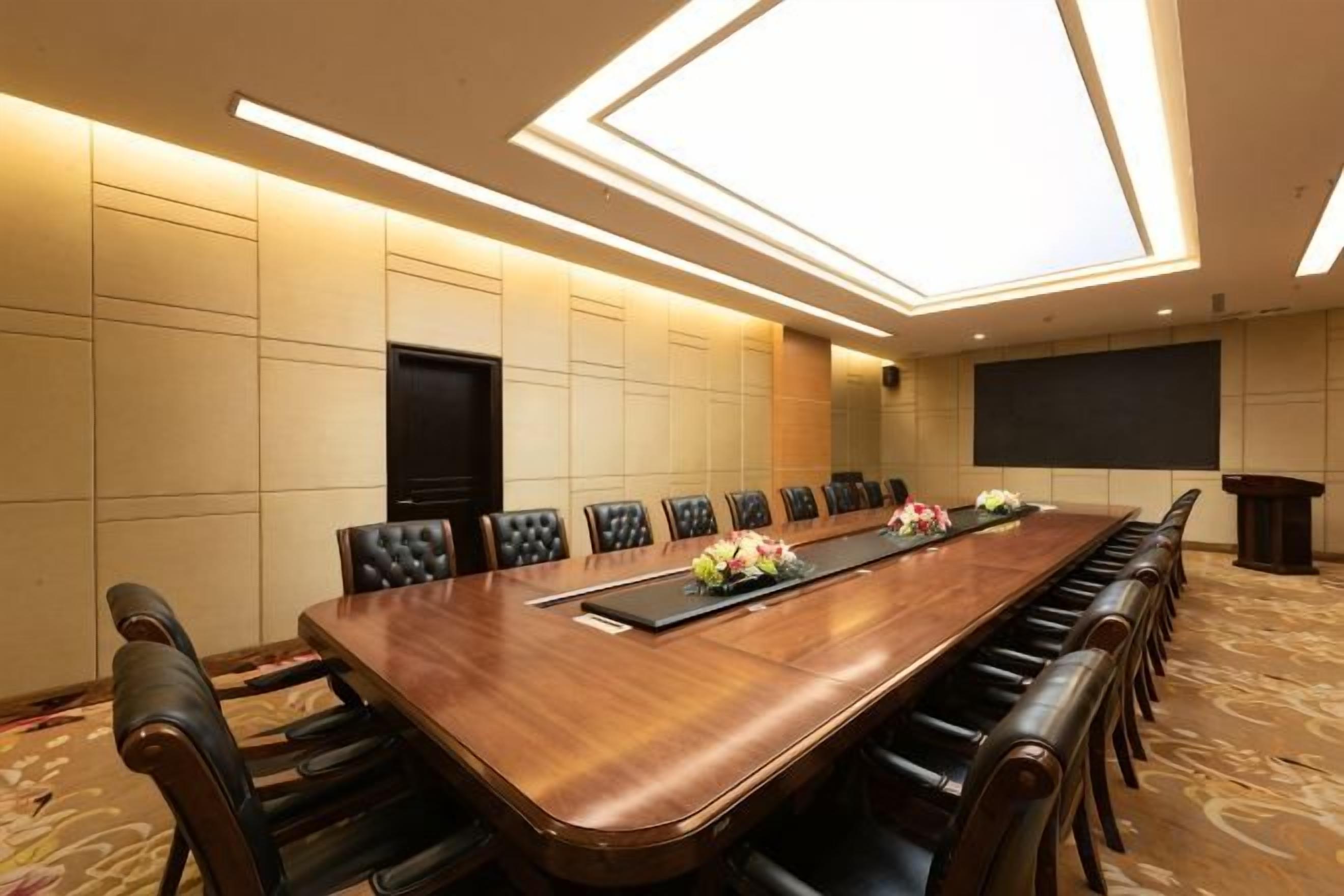 Un salón de conferencias con una larga mesa, sillas, una pantalla de proyector y un televisor.