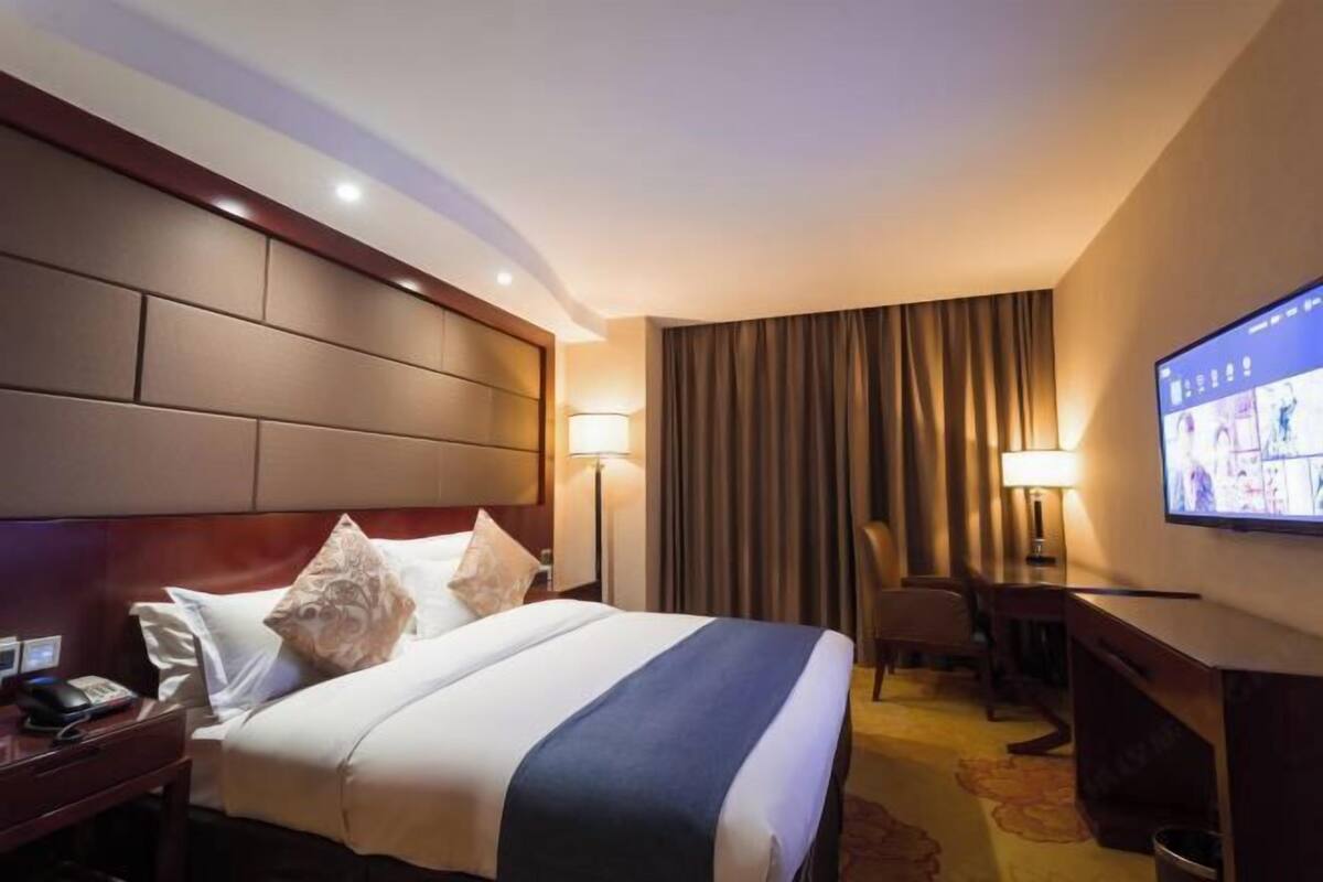 Habitación de hotel con cama, escritorio, silla, televisor y lámpara.