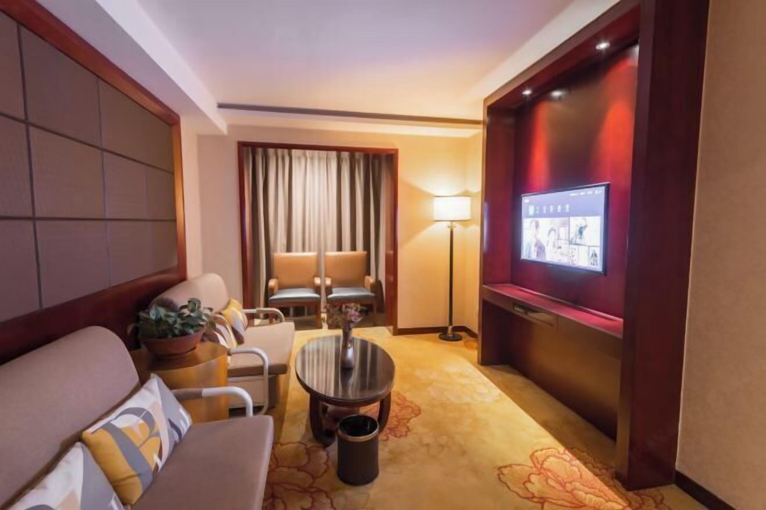 Een hotelkamer met een bank, fauteuils, een kleine tafel, een televisie en een lamp.