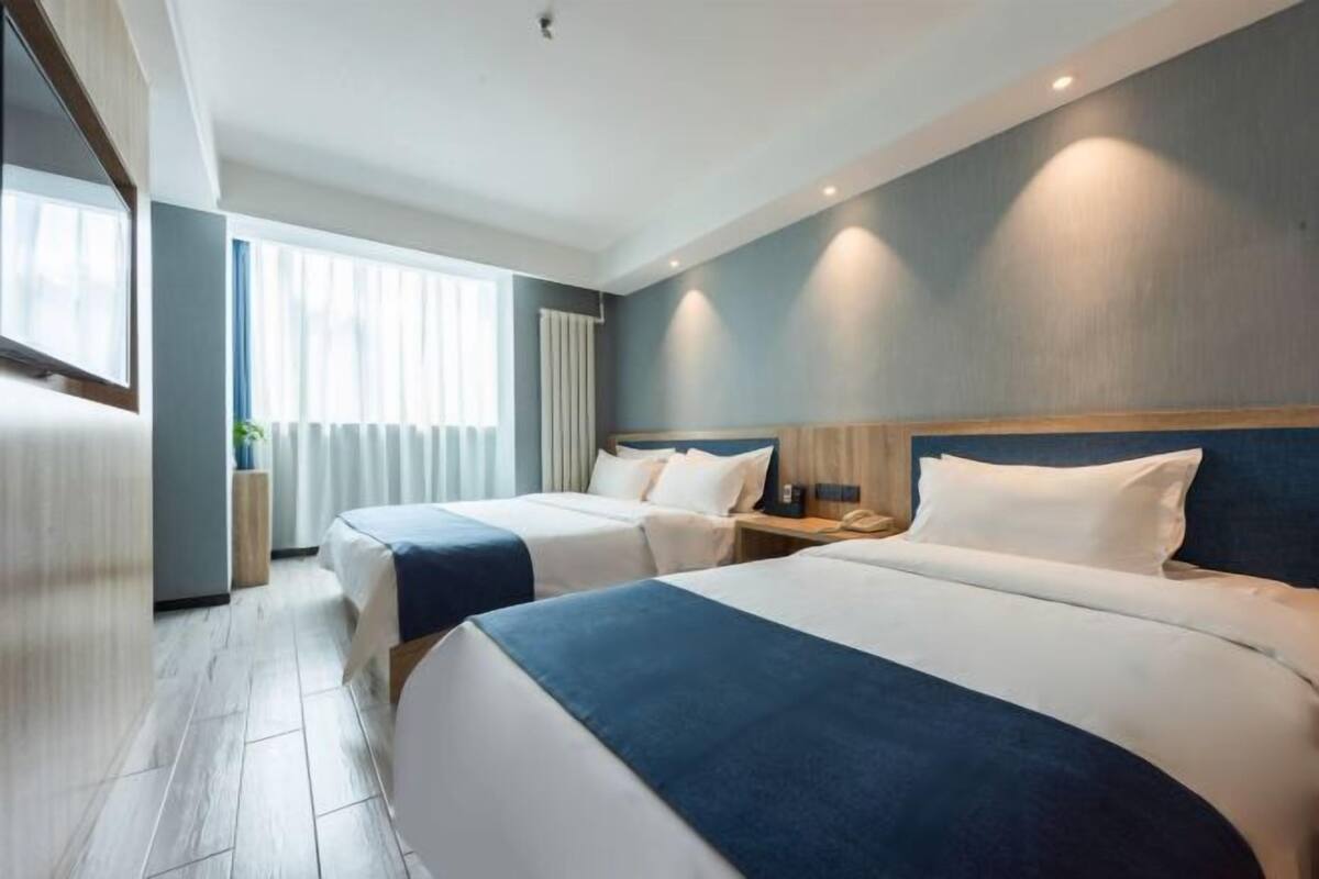 Habitación de hotel con dos camas, un ventanal con cortinas, una mesita de noche con lámpara y un teléfono en la pared.