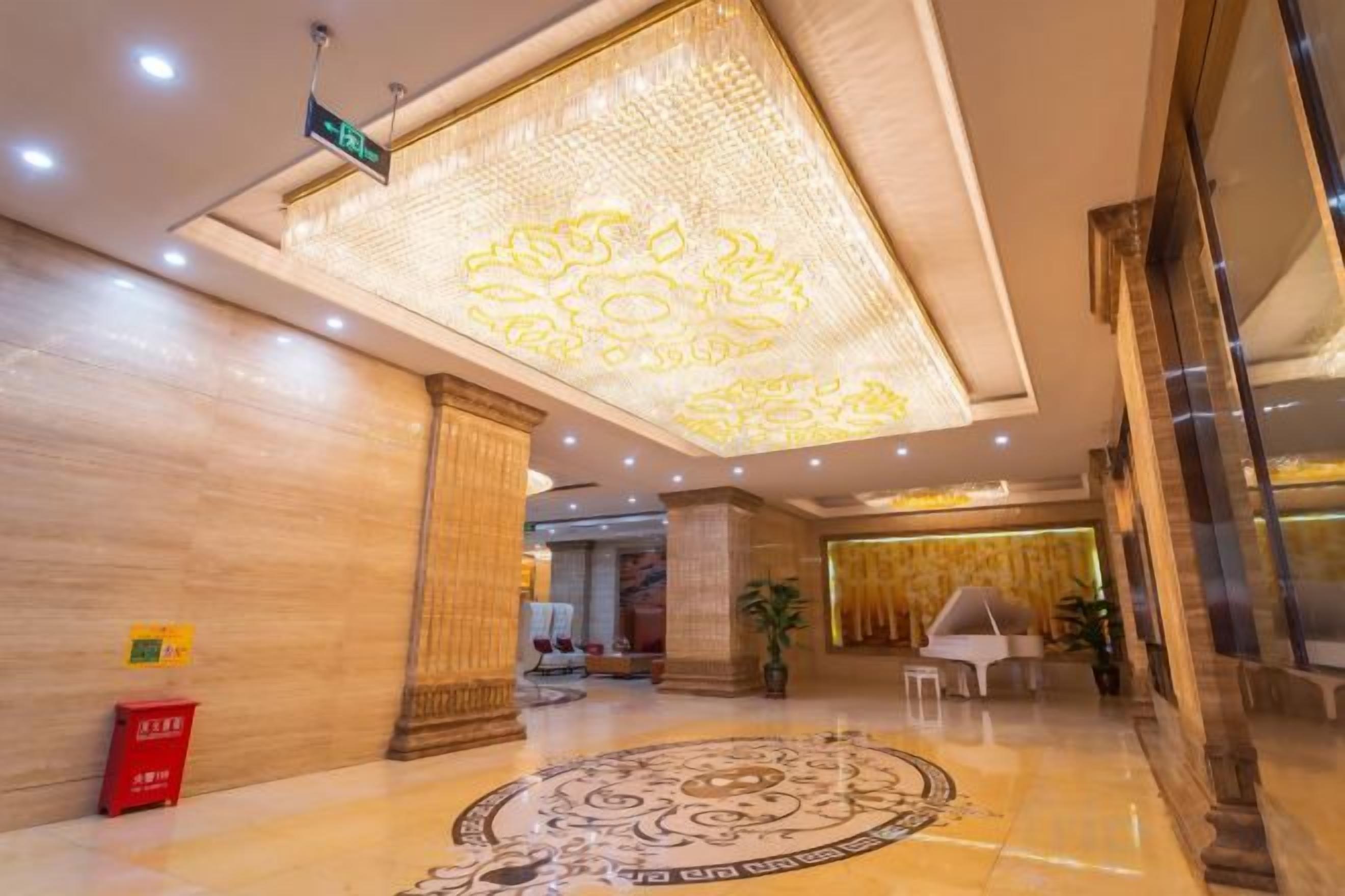 A hotel lobby with a patterned carpet, a chandelier, and a reception desk.